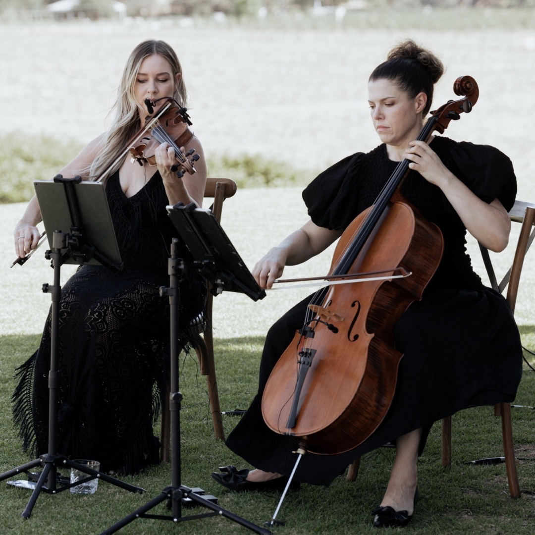 Image: 2 people playing string instruments outside.